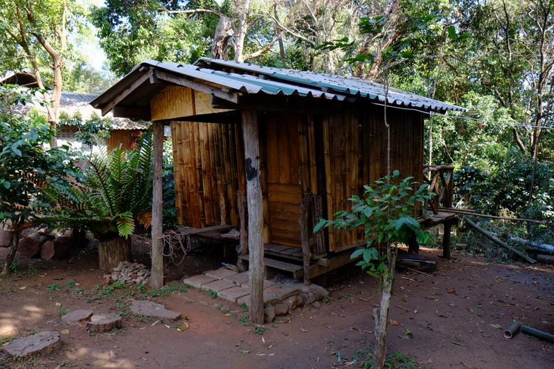 Small wooden hut with a sloped metal roof in a forest setting at Khun Chang Kian Village.