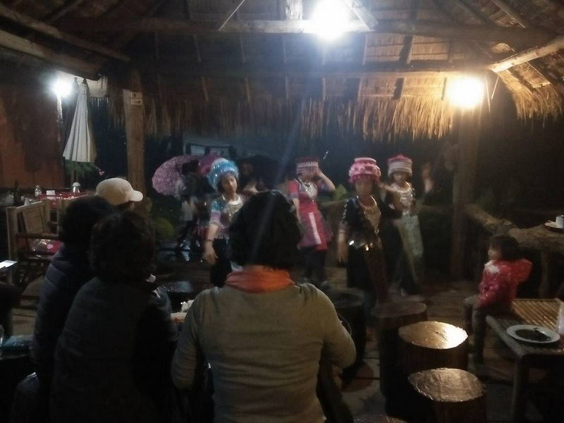 Performers in traditional costumes dancing indoors with audience watching at Khun Chang Kian Village.