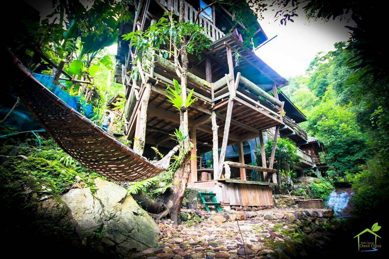 Stilt House in Lush Forest at Ban Mae Kanpong Wooden stilt house among lush green trees with stream and rocky ground nearby at Ban Mae Kanpong.