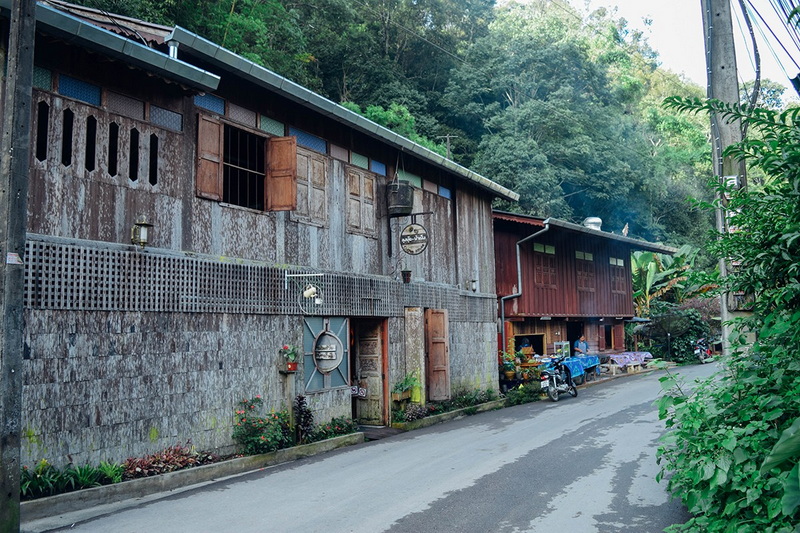 Rustic buildings with metal and wooden exteriors along a small mountain road at Ban Mae Kanpong.