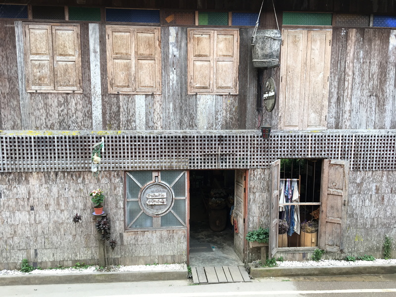 Weathered wooden building with open entrance, plants, and hanging laundry exterior at Ban Mae Kanpong.