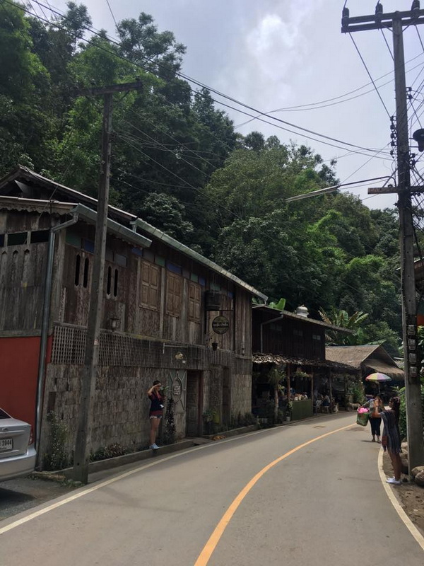 Village Street Scene at Mae Kanpong Village Street with wooden houses and people walking beside a forested hillside at Mae Kanpong Village.