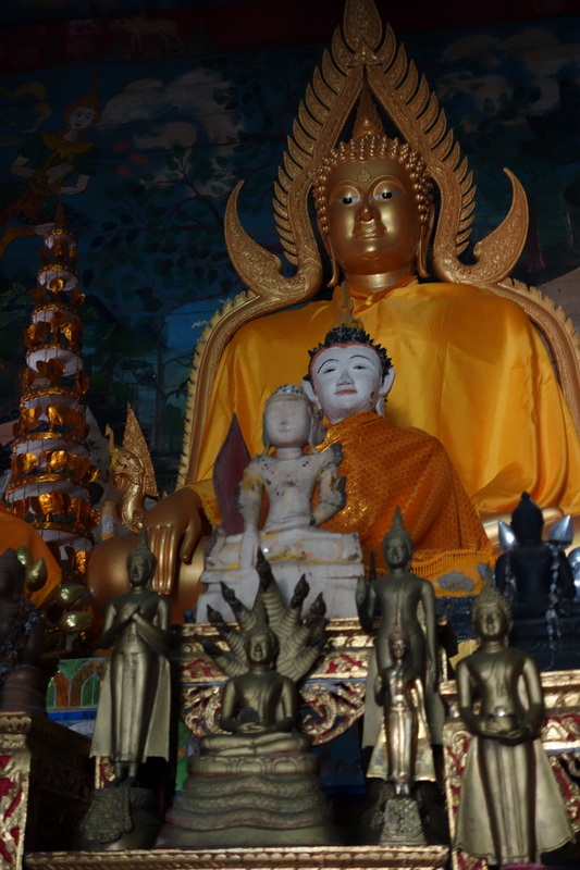 Large golden Buddha statue with smaller statues in an ornate temple setting at Mae Kanpong Village.