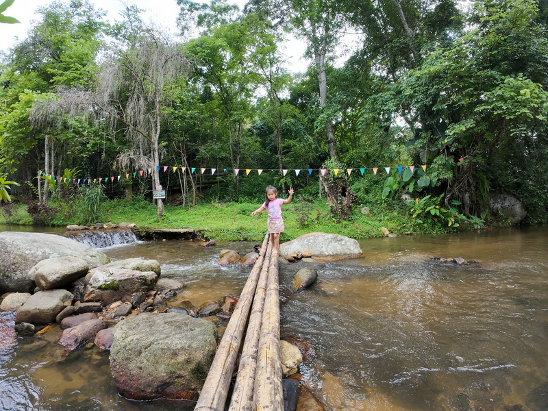 Girl standing on a wooden bridge over a flowing stream in a lush forest at Pang Hi Village.