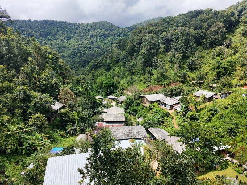 Mountain Village Scene at Pang Hi Village A mountain landscape with small wooden houses among dense greenery and clouds above at Pang Hi Village.