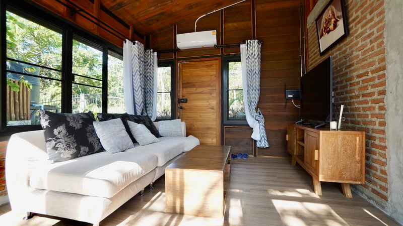 Cozy Wooden Interior at Pang Hi Village Interior of a wooden house with sofa, windows, and TV, overlooking greenery at Pang Hi Village.