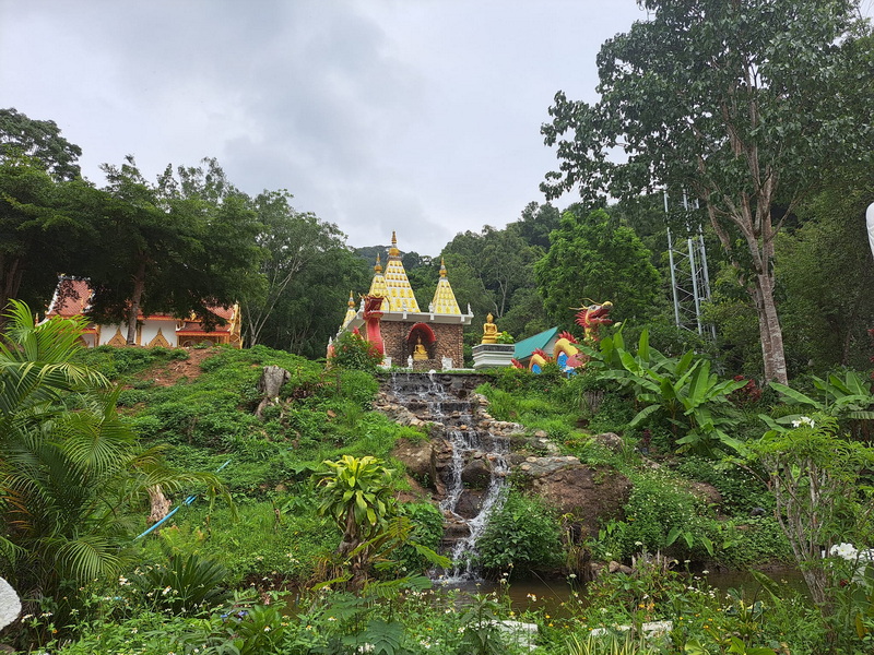 Waterfall and Temple Scene at Pang Hi Village Small waterfall flowing over rocks with a temple-like structure in lush greenery at Pang Hi Village.