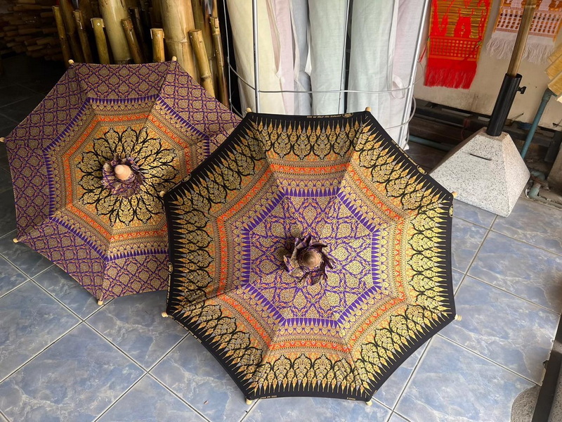 Two ornate umbrellas with floral and geometric designs on a tiled floor indoors at San Kamphaeng Village.