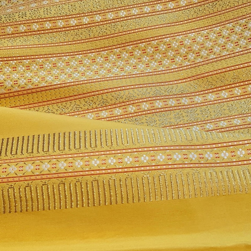 Close-up of yellow textile with detailed gold and red embroidery patterns at San Kamphaeng Village.