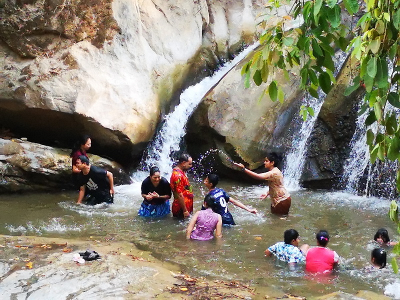 People enjoying in a small waterfall surrounded by rocks and greenery at Mae Sa Waterfall.