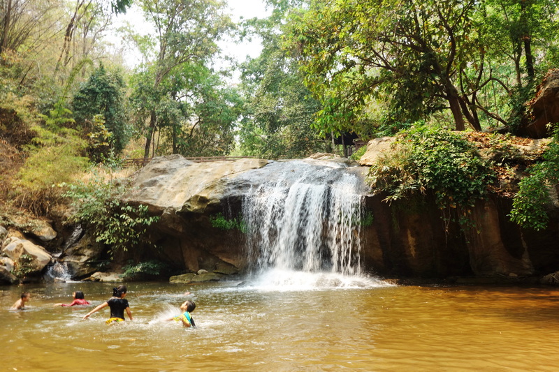 People swimming in a natural pool with a small waterfall and surrounding trees at Mae Sa Waterfall.