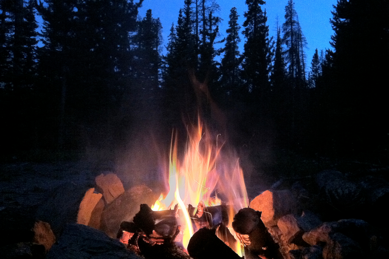 Campfire burning with flames and rocks, pine forest in the background at twilight at Chiang Mai International School Summer Camp.