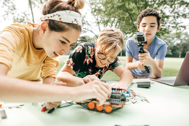 children assembling electronics outdoors with trees in the background at Nature Camp For Kids Chiang Mai.