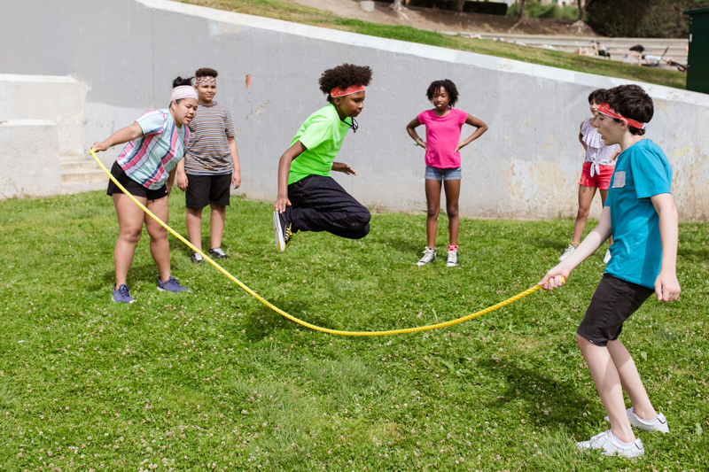Children Playing Jump Rope Outside at Teenager Camps Chiang Mai Children playing jump rope outdoors on a grassy area with onlookers nearby at Teenager Camps Chiang Mai.