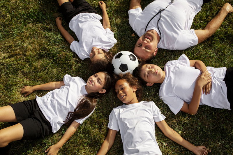 Children Playing with Soccer Ball at Kids Camp Chiang Mai Children and adult lying on grass with a soccer ball in the center during outdoor activity at Kids Camp Chiang Mai.