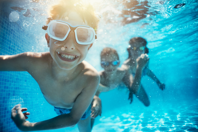 Children swimming underwater wearing goggles and smiling at Best Youth Camps In Chiang Mai.