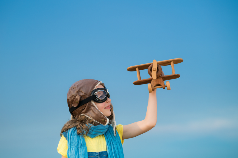 Girl with Wooden Airplane at Chiang Mai Youth Camp Girl with aviator helmet and goggles holding a wooden airplane under blue sky at Chiang Mai Youth Camp.