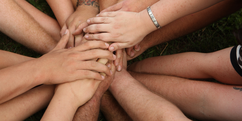 Group of diverse hands stacked together in a circle on grass at Summer Camp In Chiang Mai.