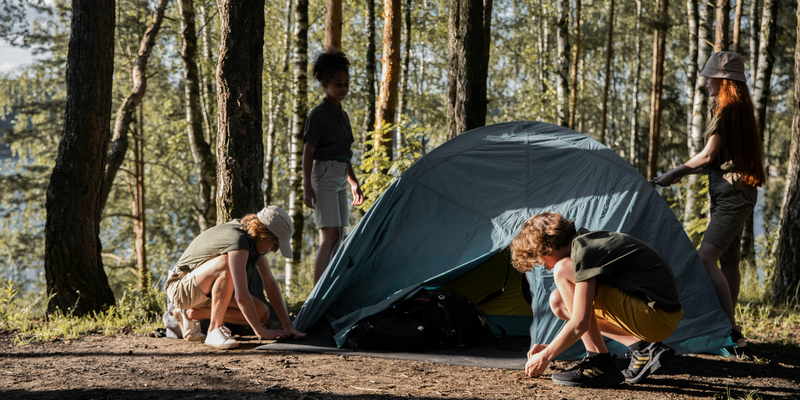 Children assembling a tent in a sunlit forest during a camping trip at Outdoor Education Camp Chiang Mai.