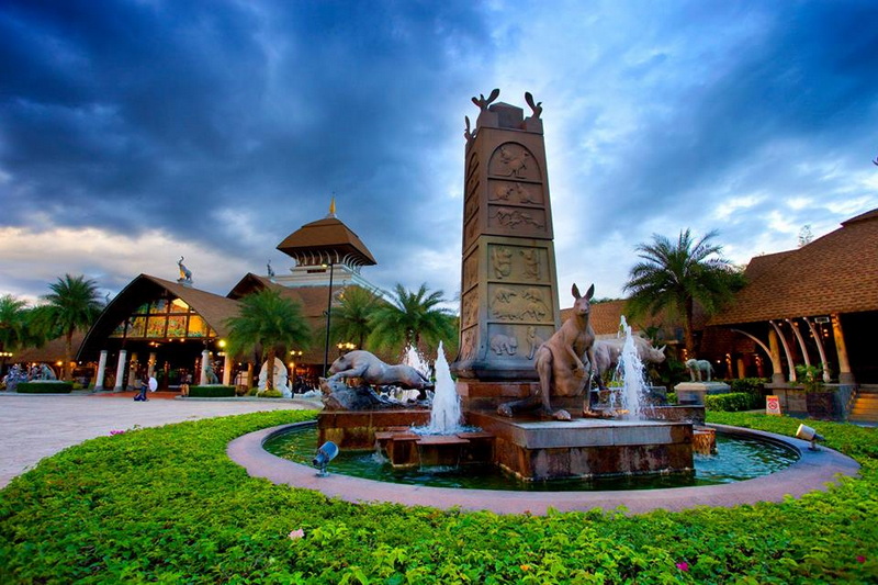Fountain with animal sculptures in front of traditional-style buildings and palm trees at Chiang Mai Night Safari.